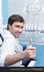 A young man in a dental chair shows thumbs up