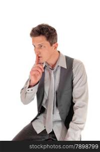 A young man in a grey shirt and vest sitting for white background withhis finger over his mouth.