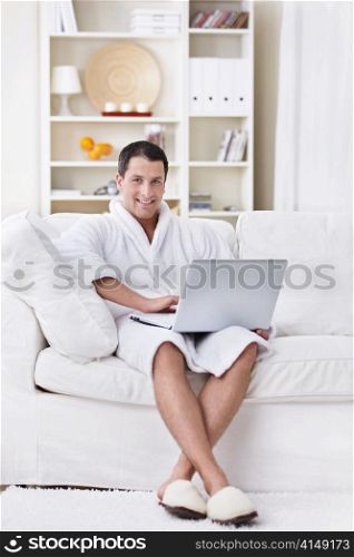 A young man in a robe with a laptop at home