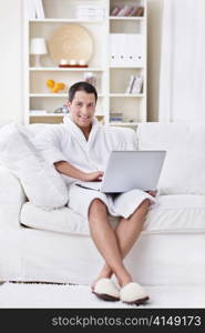 A young man in a robe with a laptop at home