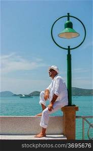 A young man in a white suit sits on the waterfront