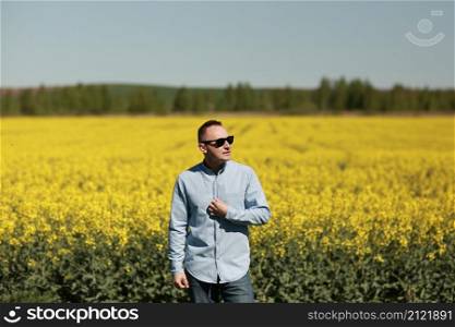A young man in sunglasses is walking and having fun through a Sunny yellow rapeseed field, the concept of travel and freedom. summer holiday background.. A young man in sunglasses is walking and having fun through a Sunny yellow rapeseed field, the concept of travel and freedom. summer holiday background