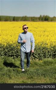 A young man in sunglasses is walking and having fun through a Sunny yellow rapeseed field, the concept of travel and freedom. summer holiday background.. A young man in sunglasses is walking and having fun through a Sunny yellow rapeseed field, the concept of travel and freedom. summer holiday background