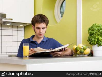 A young man in the kitchen looking at recipes.