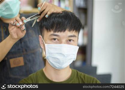 a young man is getting a haircut in a hair salon , wearing face mask for protection covid-19 , Salon safety concept