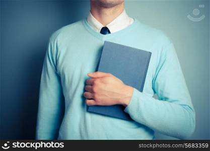 A young man is holding a big blue book