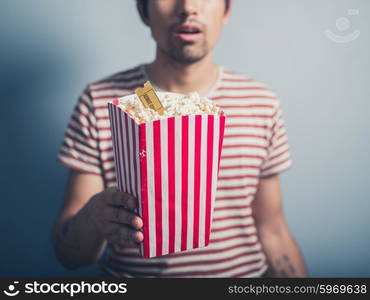 A young man is holding a box of popcorn with a cinema ticket in it