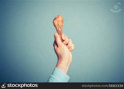 A young man is holding a roasted chicken drumstick