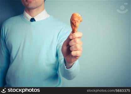 A young man is holding a roasted chicken drumstick