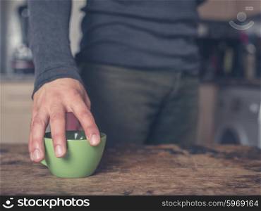 A young man is placing a cup of coffee on a table in a kitchen