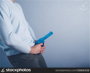 A young man is posing with a water pistol and is holding it in front of his crotch