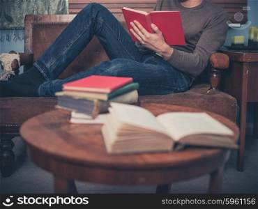 A young man is relaxing on a sofa at home and is reading a book