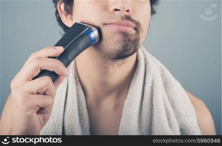 A young man is shaving off half of his beard