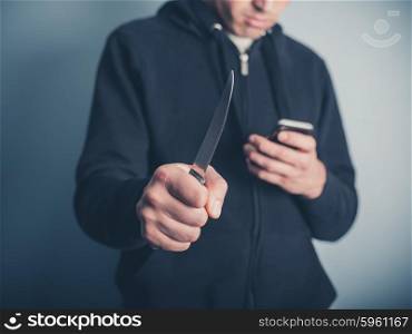 A young man is showing threatening behaviour by waving a knife whilst using a smartphone at the same time