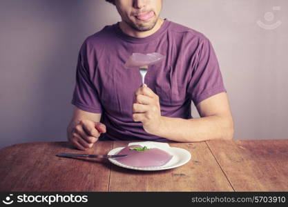 A young man is sitting at a table and eating a purple jelly pudding