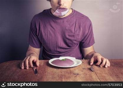 A young man is sitting at a table and eating a purple jelly pudding