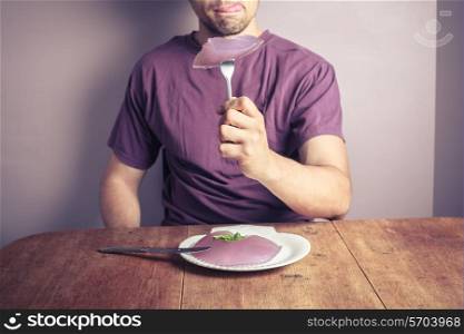 A young man is sitting at a table and eating a purple jelly pudding