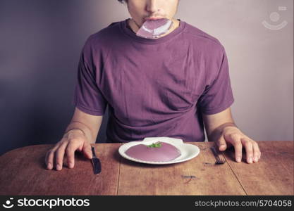 A young man is sitting at a table and eating a purple jelly pudding