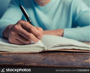 A young man is sitting at a table and is writing in a notebook