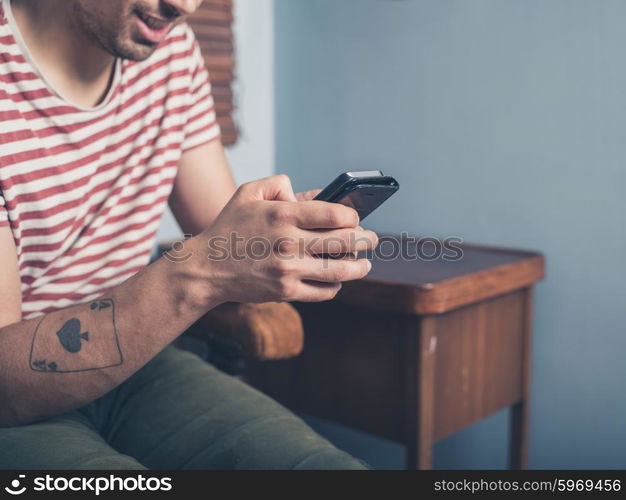 A young man is sitting on a sofa and is using a smart phone at home