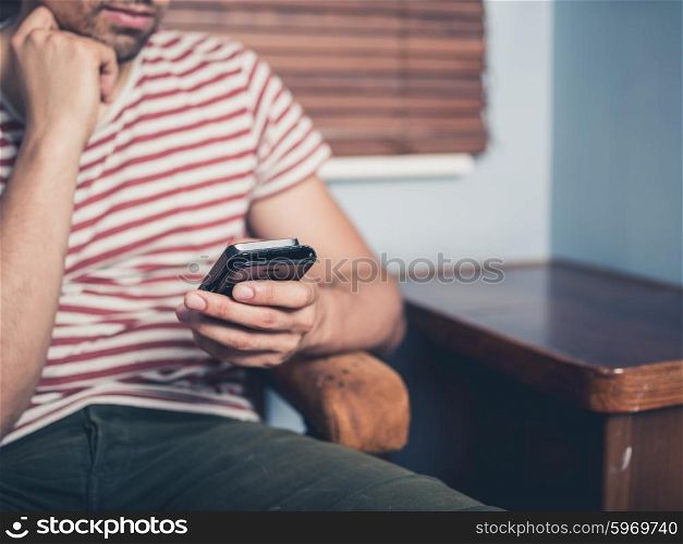 A young man is sitting on a sofa and is using a smart phone at home