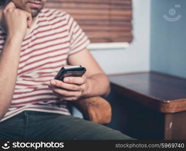 A young man is sitting on a sofa and is using a smart phone at home