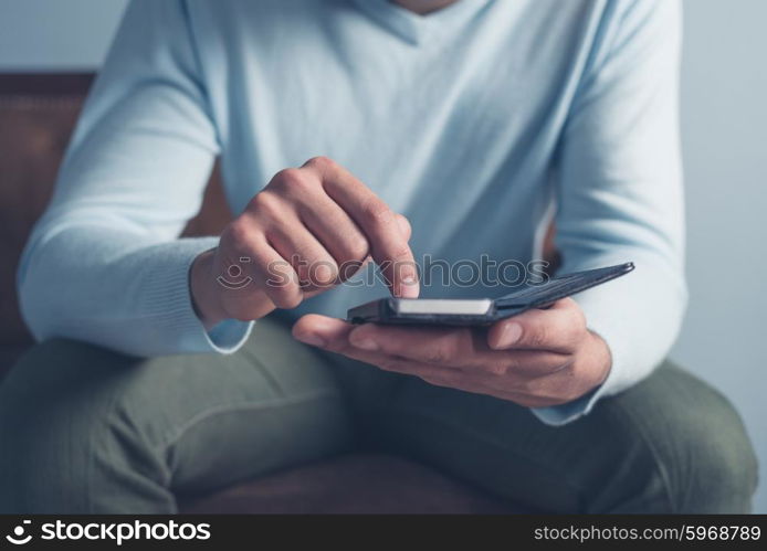 A young man is sitting on an old antique sofa and is using a smart phone