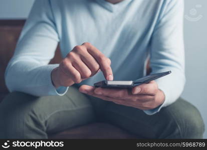 A young man is sitting on an old antique sofa and is using a smart phone