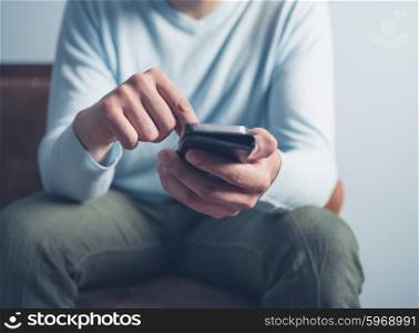 A young man is sitting on an old antique sofa and is using a smart phone