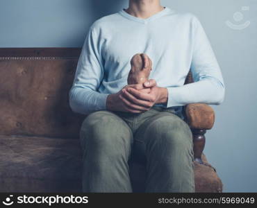 A young man is sitting on an old sofa and is holding a strange looking sweet potato