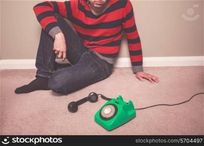 A young man is sitting on the floor and is desperately waiting for a phone call