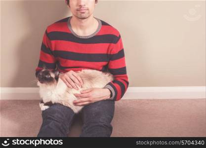 A young man is sitting on the floor and petting his cat