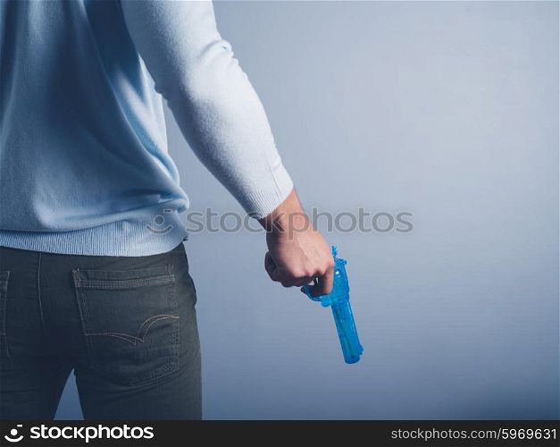 A young man is standing against a blue background and is posing with a water pistol