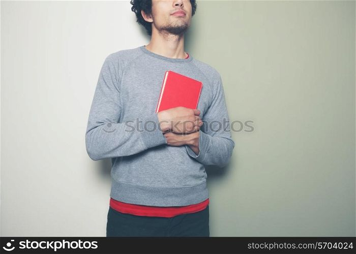 A young man is standing against a split colored green and white background and holding a red book