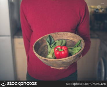 A young man is standing in a kitchen with a bowl of pak choi and red pepper