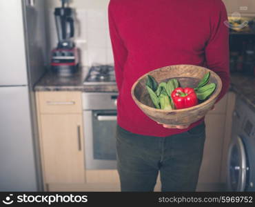 A young man is standing in a kitchen with a bowl of pak choi and red pepper