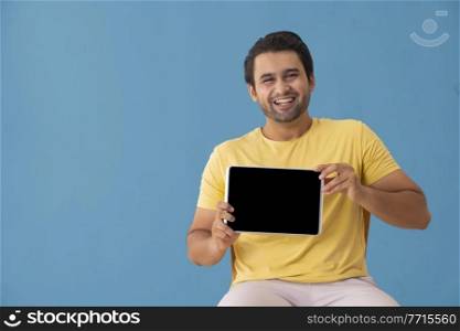 A young man laughing while showing a tablet phone in his hand.