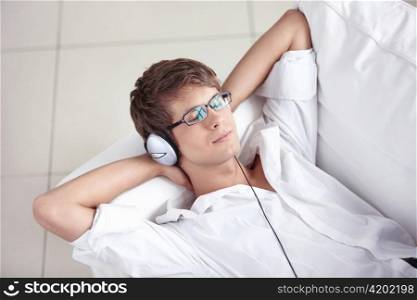 A young man listening the music in the headphones on the sofa