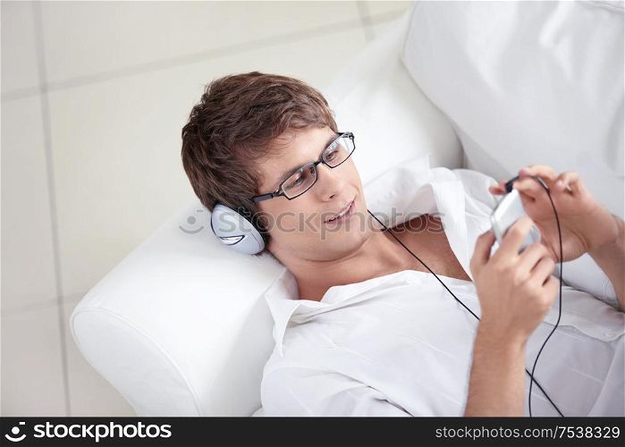 A young man listens to the headphones on the sofa