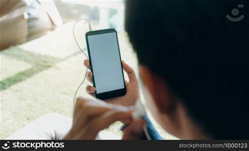 A young man lying down on a soft cushion feel relaxed and listen to online music from mobile phone in his house