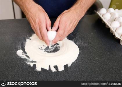A young man making pasta at home in an apartment kitchen - Cracking an egg into the flour to be mixed by hand on the counter