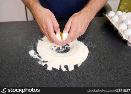 A young man making pasta at home in an apartment kitchen - Cracking an egg into the flour to be mixed by hand on the counter