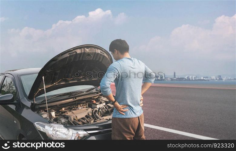 A young man near a broken car with an open hood on the roadside.