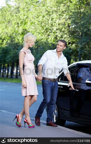 A young man opens the car door in front of a girl