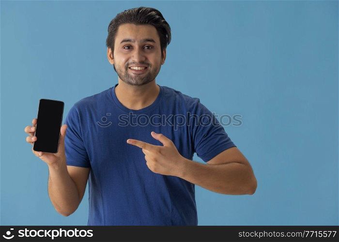 A young man pointing towards mobile phone in his hands.