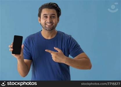A young man pointing towards mobile phone in his hands.