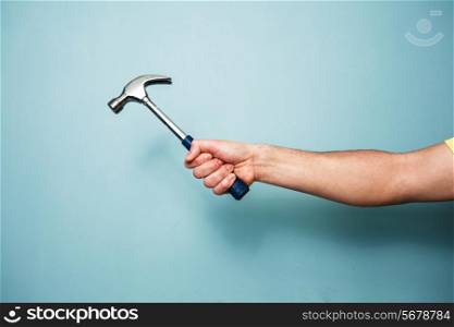 A young man&rsquo;s hand is holding a hammer against a blue wall