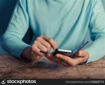 A young man sitting at a table is using a smart phone