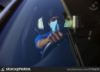A young man sitting in his car with face mask.