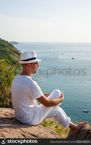 a young man sitting on a rock and looking at the sunset of Phuket